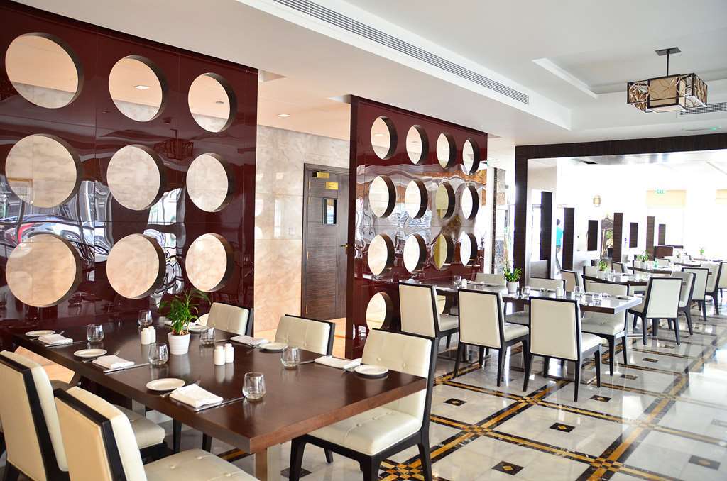 Jannah Burj Al Sarab Hotel Abu Dhabi Exterior foto The photo shows a modern restaurant interior. It features a series of tables with elegant place settings and comfortable chairs. The walls are decorated with a unique design, displaying round mirrors or circular elements set in a polished brown panel