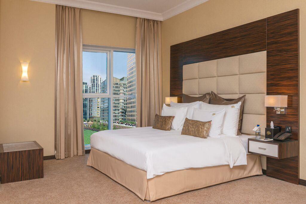 Jannah Burj Al Sarab Hotel Abu Dhabi Exterior foto The photo shows a well-decorated hotel room featuring a large bed with white bedding and decorative pillows. The walls are painted in a warm color, and there are modern wooden accents. On one side, there are light fixtures, and beside the bed, there 